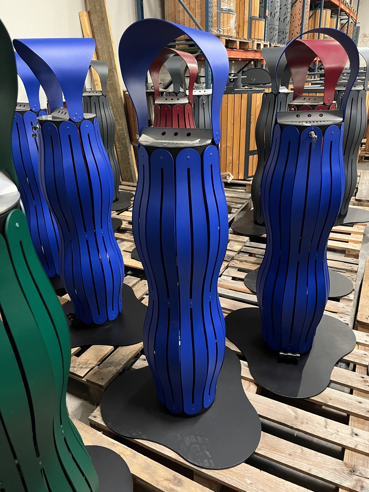 Une s&eacute;rie de cendriers bleus, rouges, verts et anthracite pos&eacute;s sur palettes dans l&rsquo;atelier, coiffes mont&eacute;es